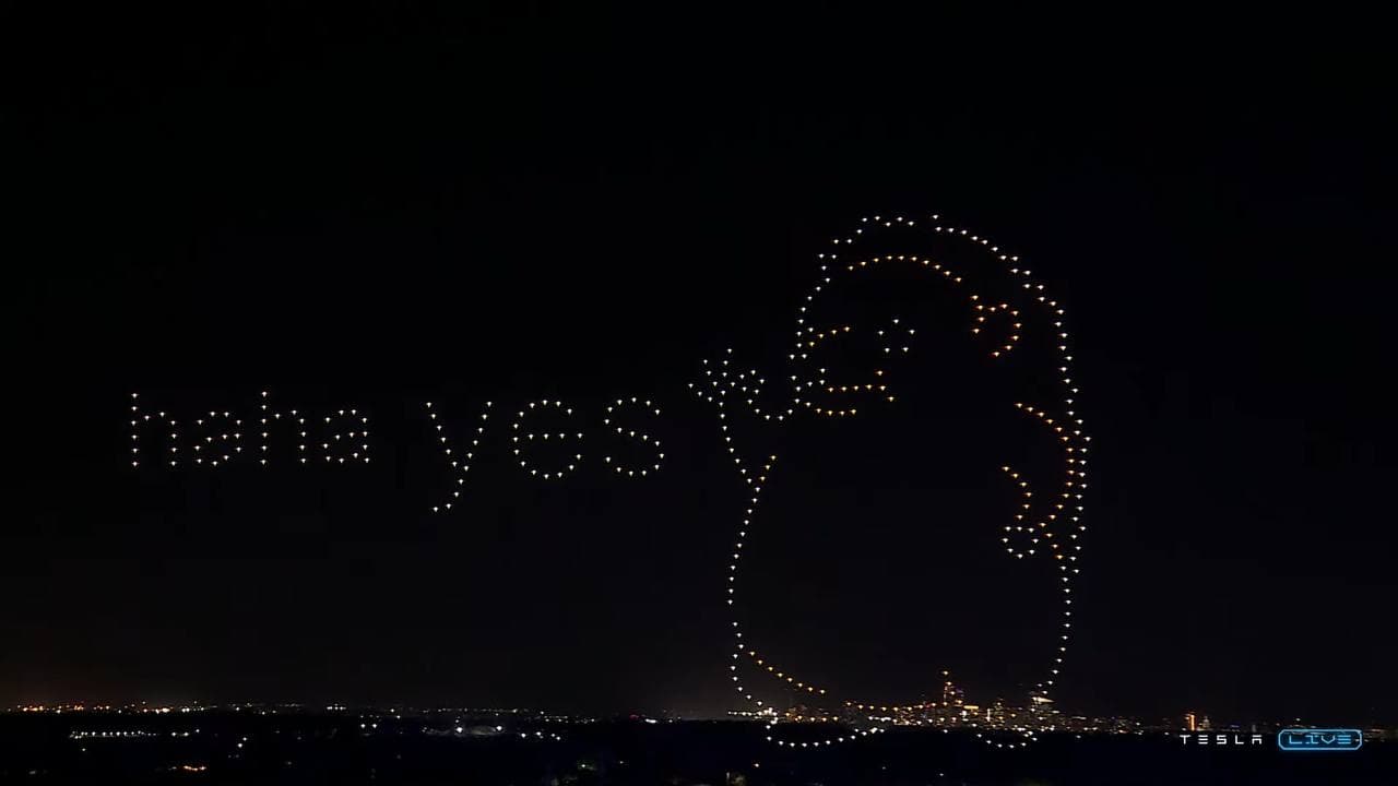 Night drone light show forming the Haha Yes hedgehog above a city skyline